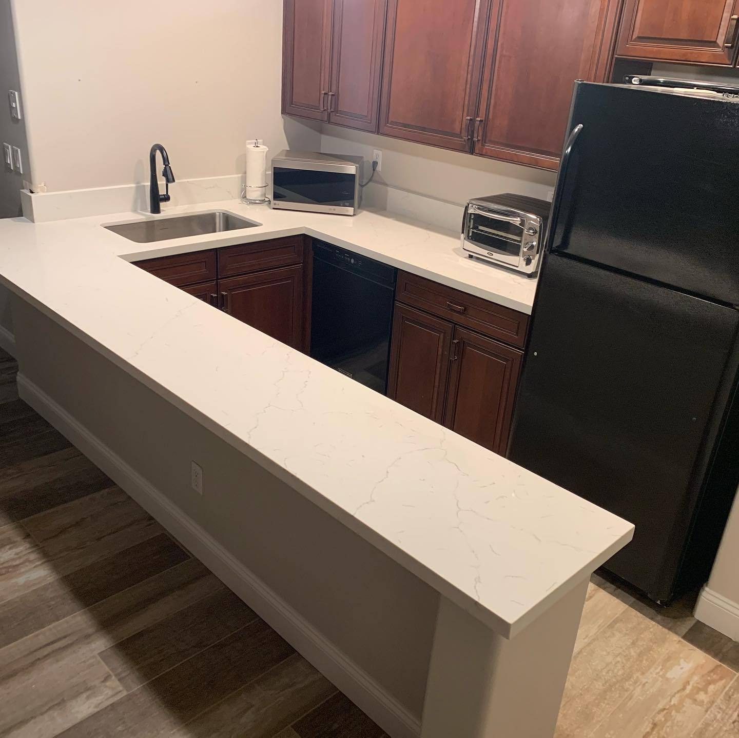 VM Stoneworks — White quartz bar-height counter with cherry cabinets