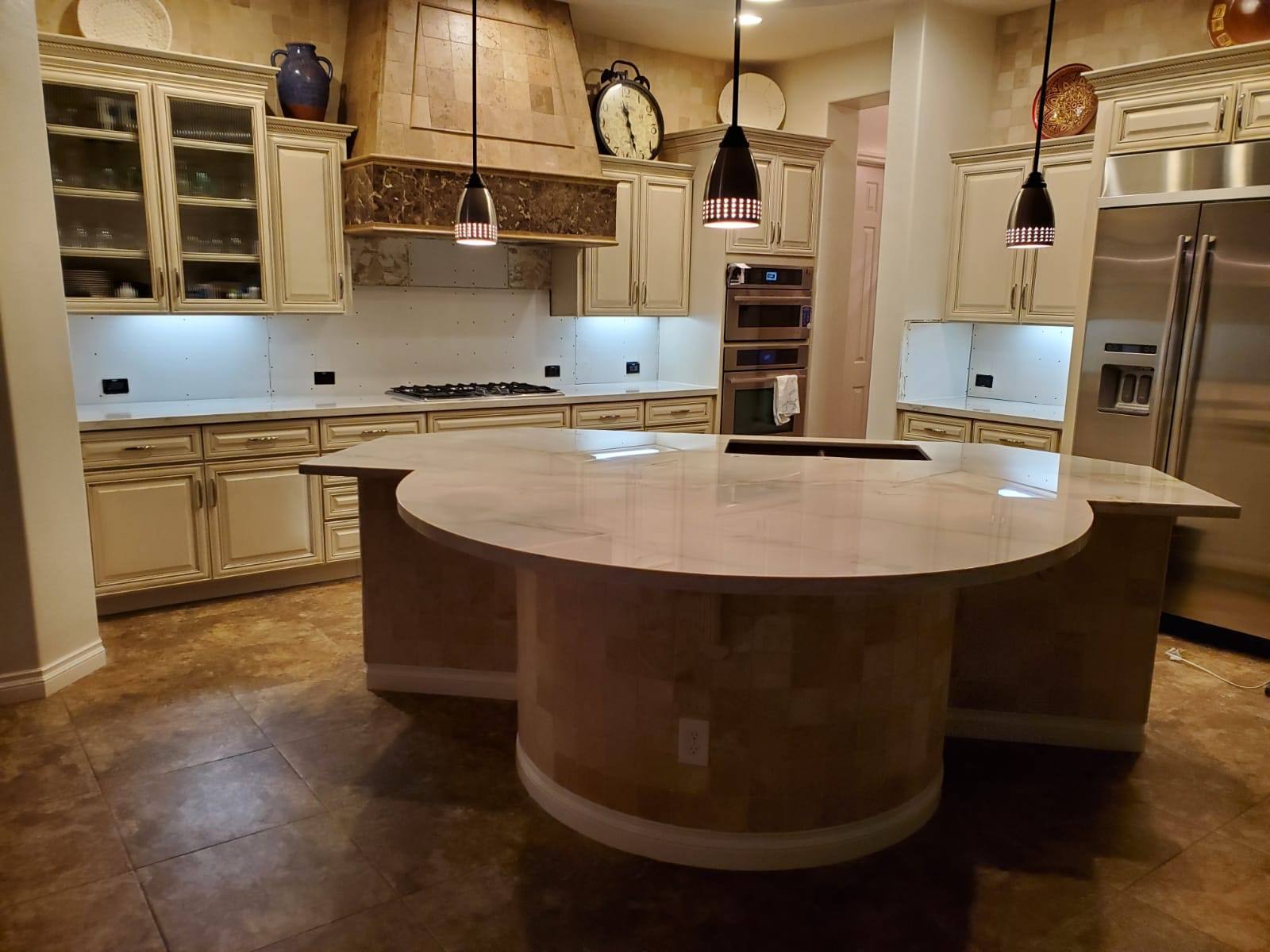 VM Stoneworks — Curved marble-look island in a travertine-accented kitchen